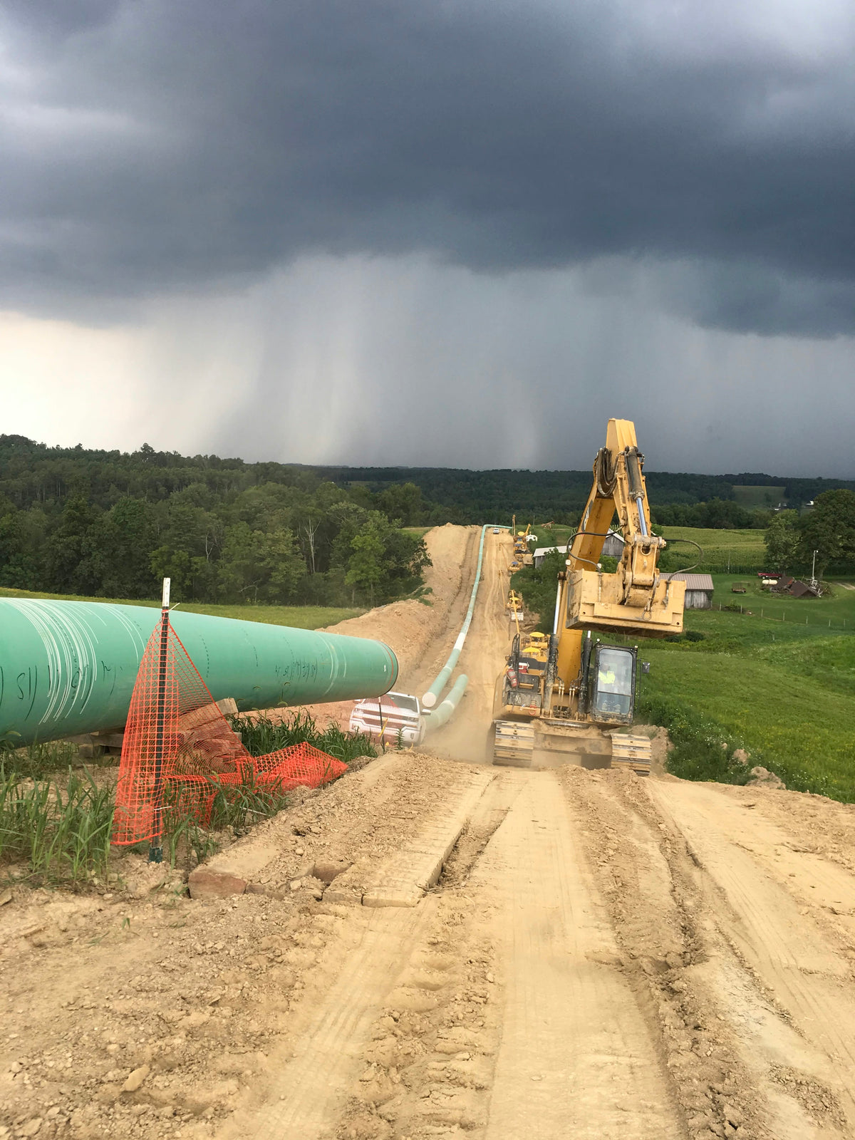 Pipeline right-of-way with green FBE-coated pipe and excavator under a storm